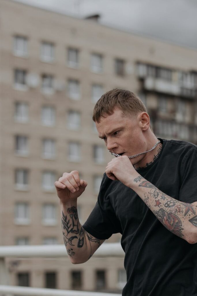 Man with tattoos shadow boxing outdoors in urban setting.
