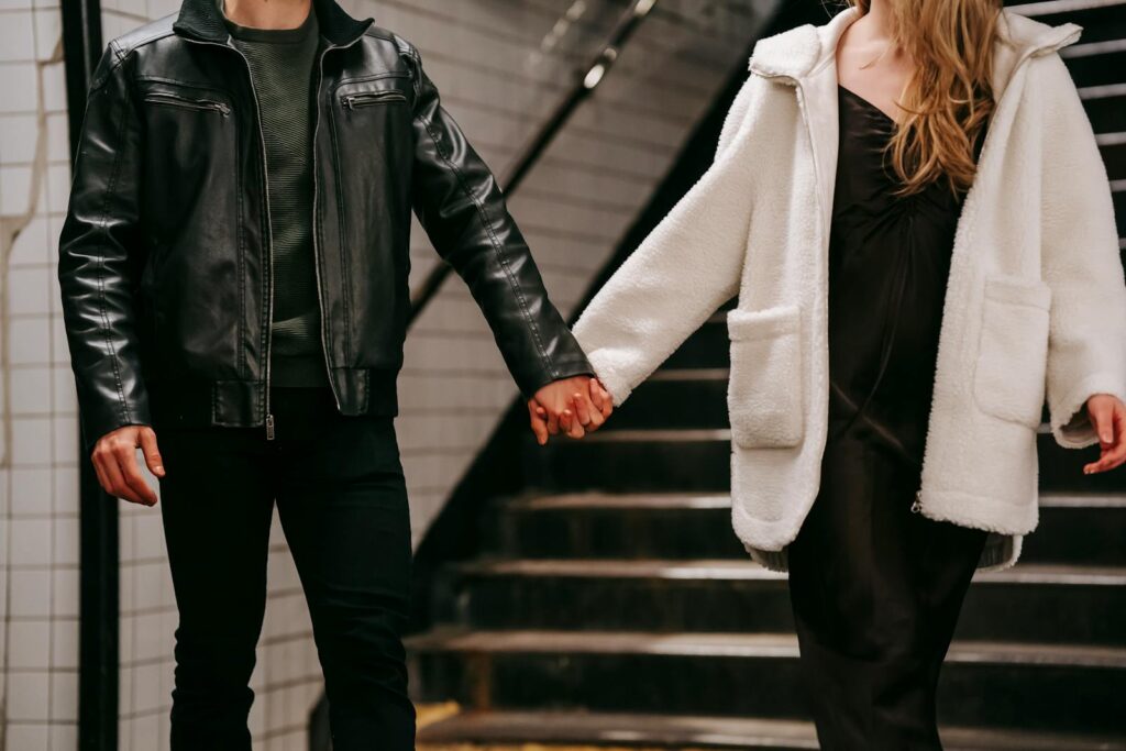 A couple in warm outerwear holding hands on a subway staircase, emphasizing affection.