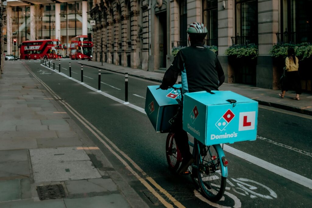 Delivery person on a bicycle in urban city with iconic red double-decker buses and historical buildings.