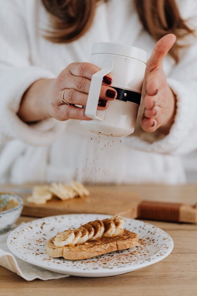 A close-up of a person sprinkling cinnamon powder over banana slices on toast.