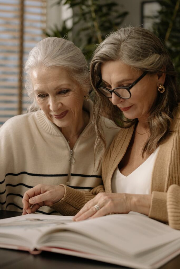 Two senior women enjoy reading a book together, creating a warm and cozy atmosphere indoors.