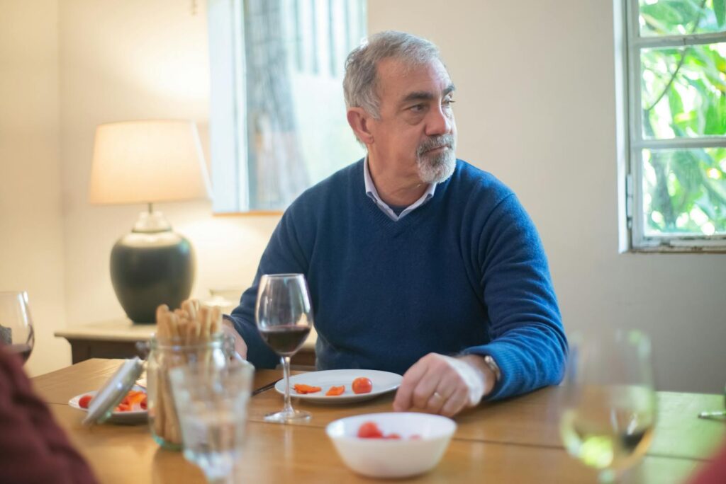 Elderly man in blue sweater enjoying a meal with wine indoors in Portugal.