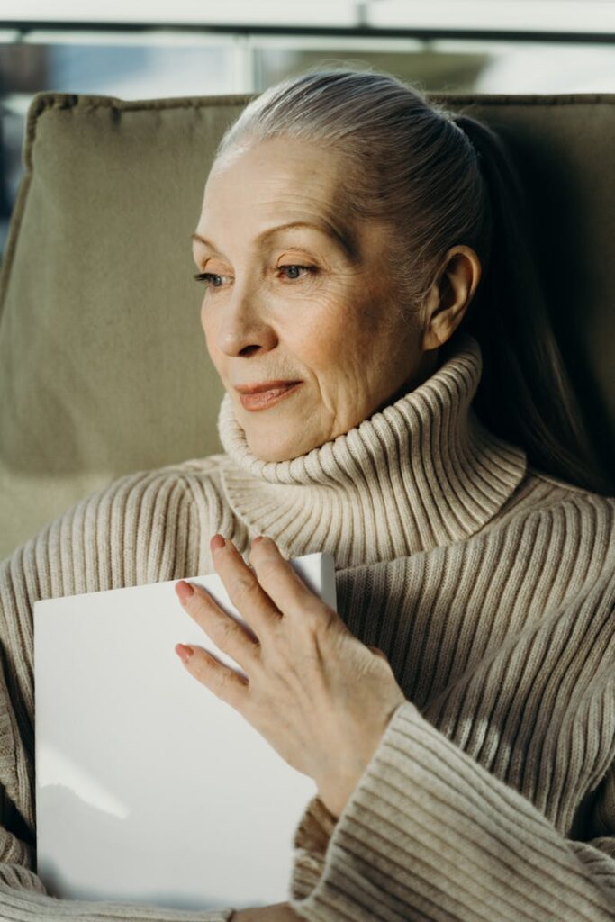 Elegant elderly woman with grey hair holding a book indoors, exuding tranquility.
