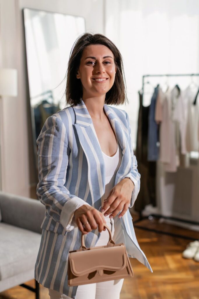 Smiling woman in blue striped blazer holding a handbag indoors.