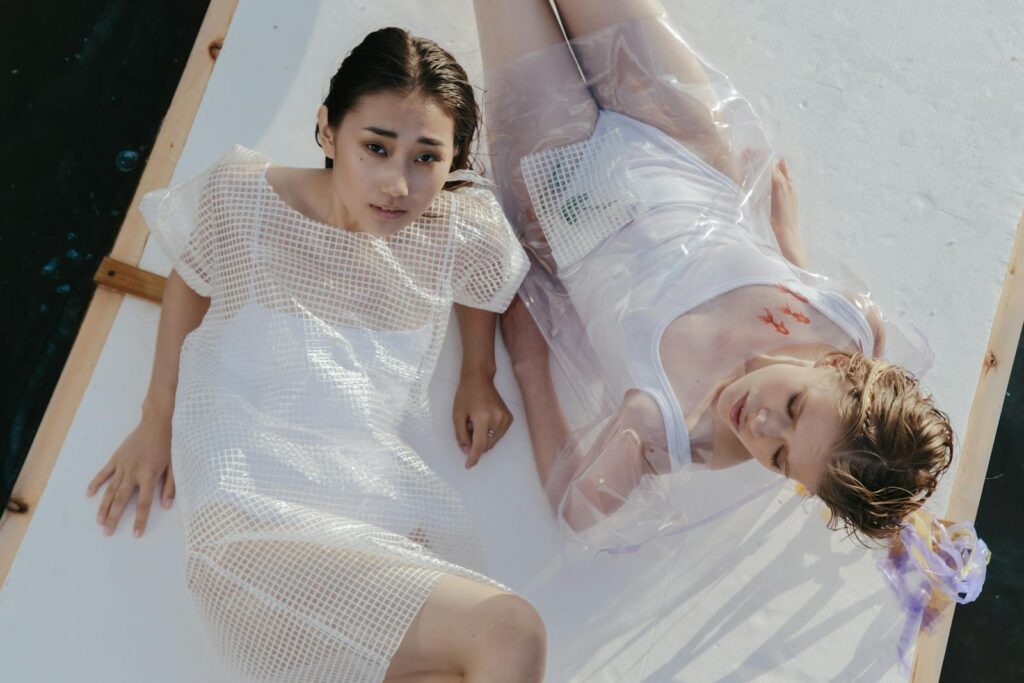 Two women in modern fashion pose on a raft, blending with water reflections for a unique conceptual art photo.