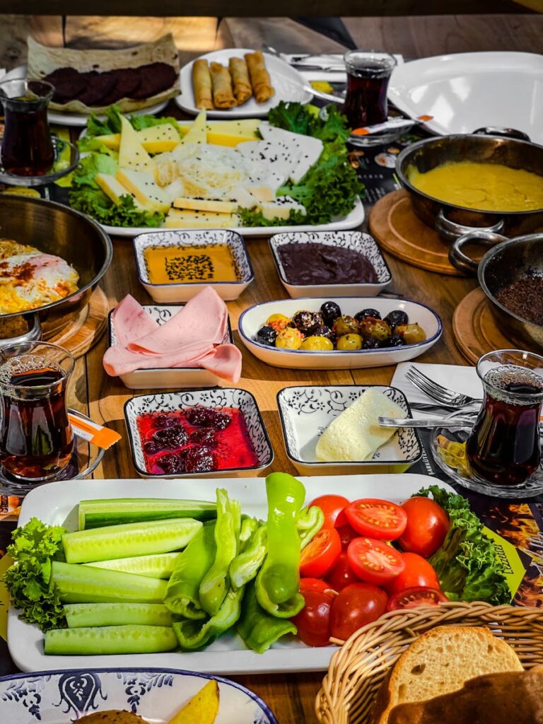 Vibrant Turkish breakfast spread with fresh vegetables, cheeses, jams, and hot tea served on a rustic wooden table.