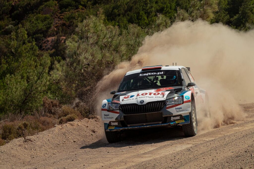 High-speed rally car kicking up dust on a rugged outdoor track, showcasing thrilling motorsport action.