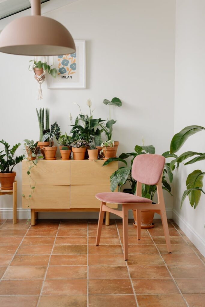 A cozy indoor setting featuring a pink chair and diverse houseplants on a terracotta floor.