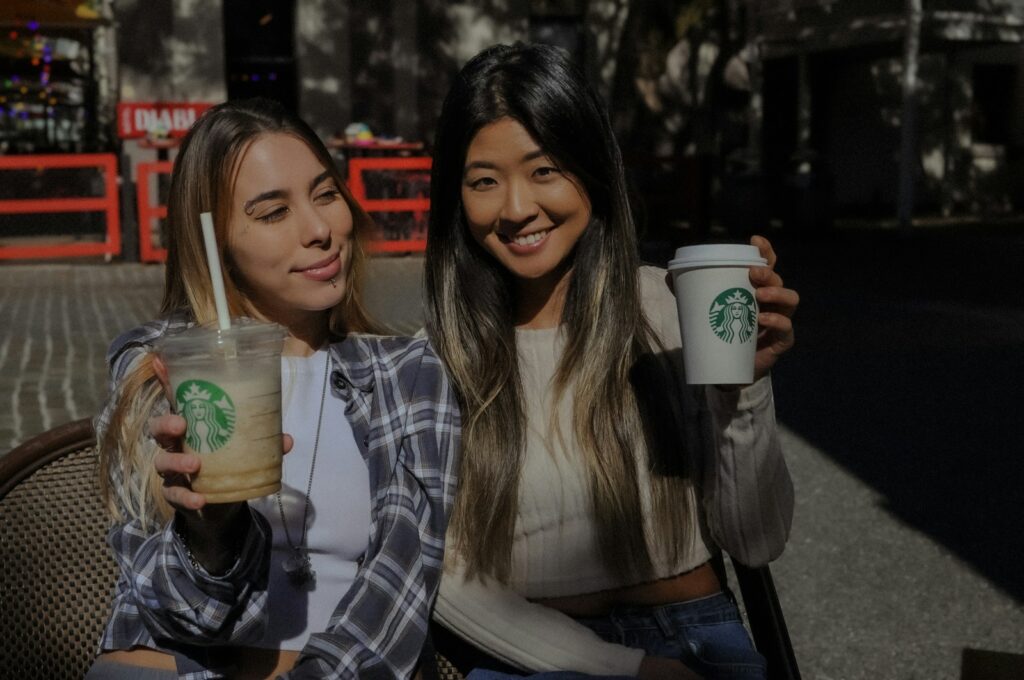 Two women sitting on a bench holding starbucks drinks