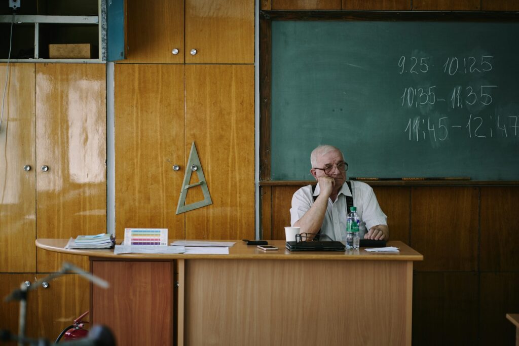 A teacher sits at his desk in a classroom.