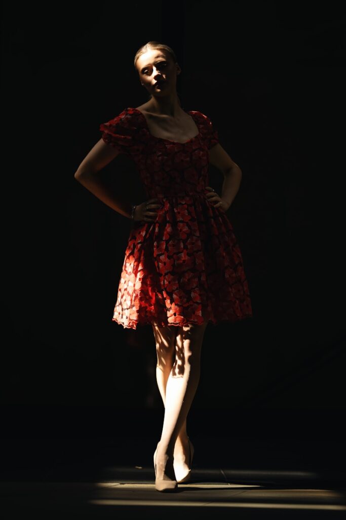 A dancer poses in a spotlit red dress.