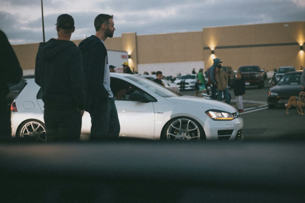 man in black suit standing beside white sedan