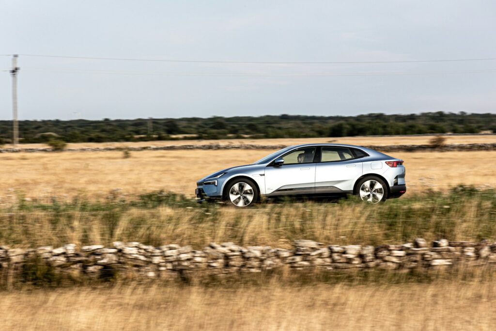 A silver car drives through a rustic field.