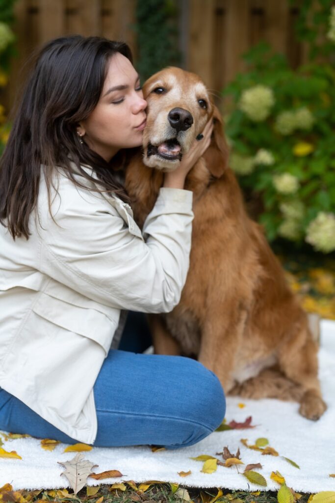 A woman sitting on the ground kissing a dog