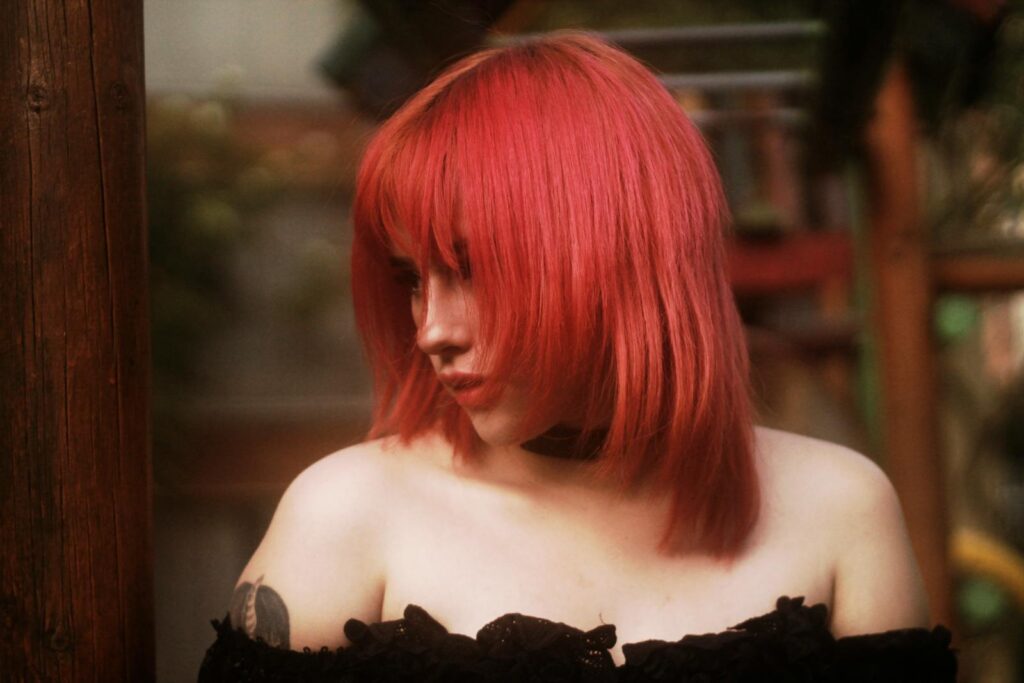 A redheaded woman in fashionable black attire poses with a thoughtful expression outdoors.