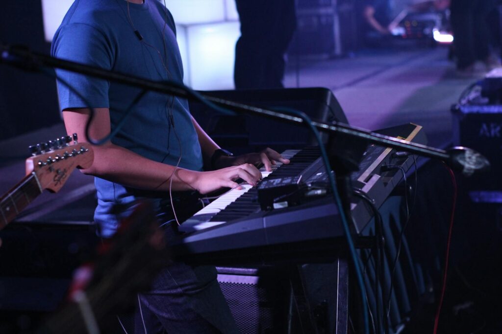 A musician performs on a keyboard during a dynamic live concert, surrounded by instruments.