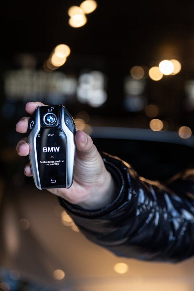 A close-up of a human hand holding a sleek black car key fob indoors.