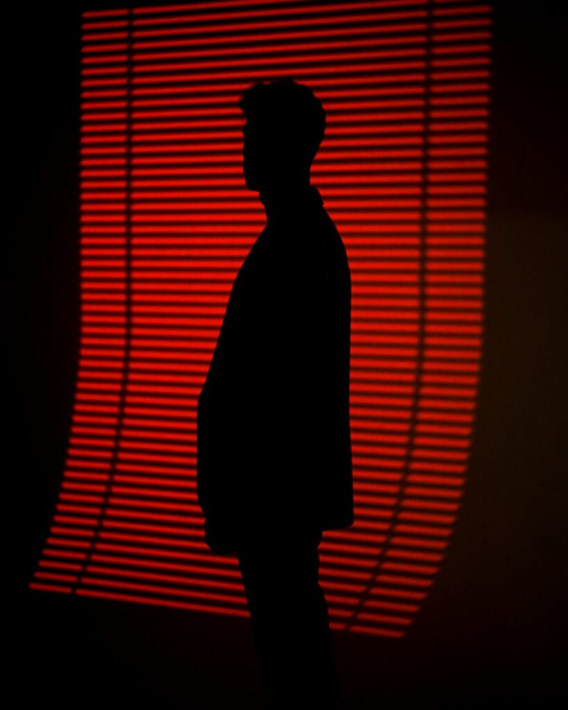 A silhouette of a person standing in front of a striking red light backdrop with horizontal lines.
