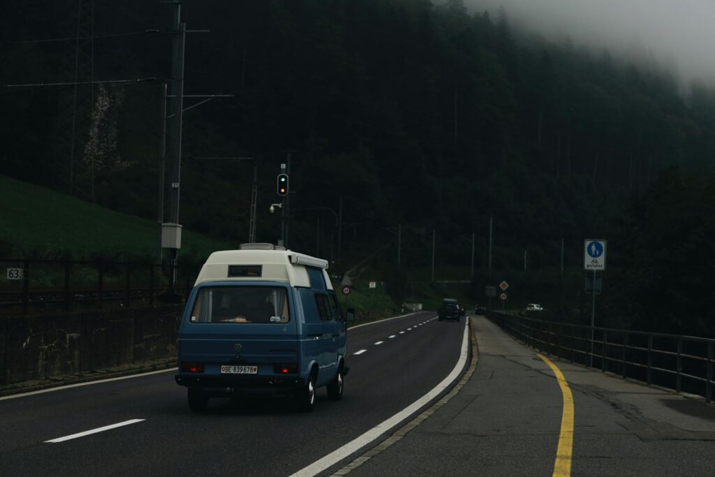 A blue camper van traveling on a misty road, surrounded by a foggy forest.