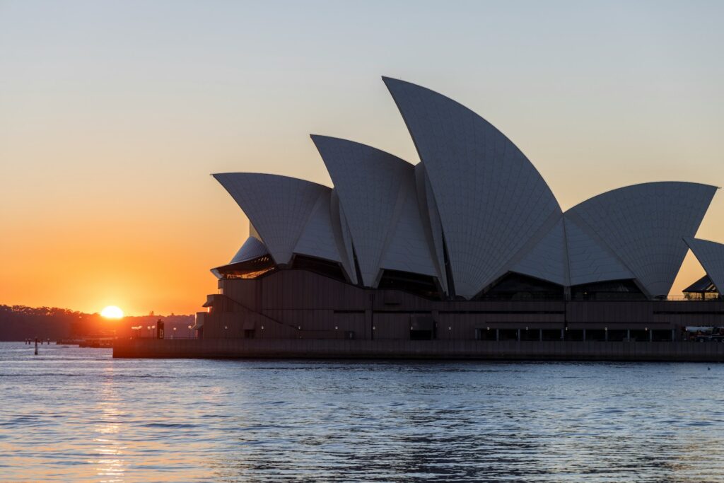 the sun is setting over the sydney opera house