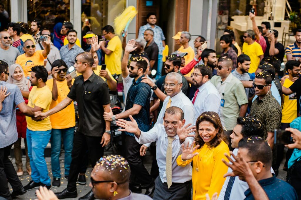 Colorful street parade featuring joyful crowds and political figures in a lively city setting.