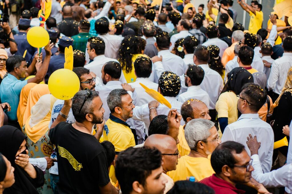 A vibrant street rally featuring a diverse and lively crowd with yellow confetti and balloons.