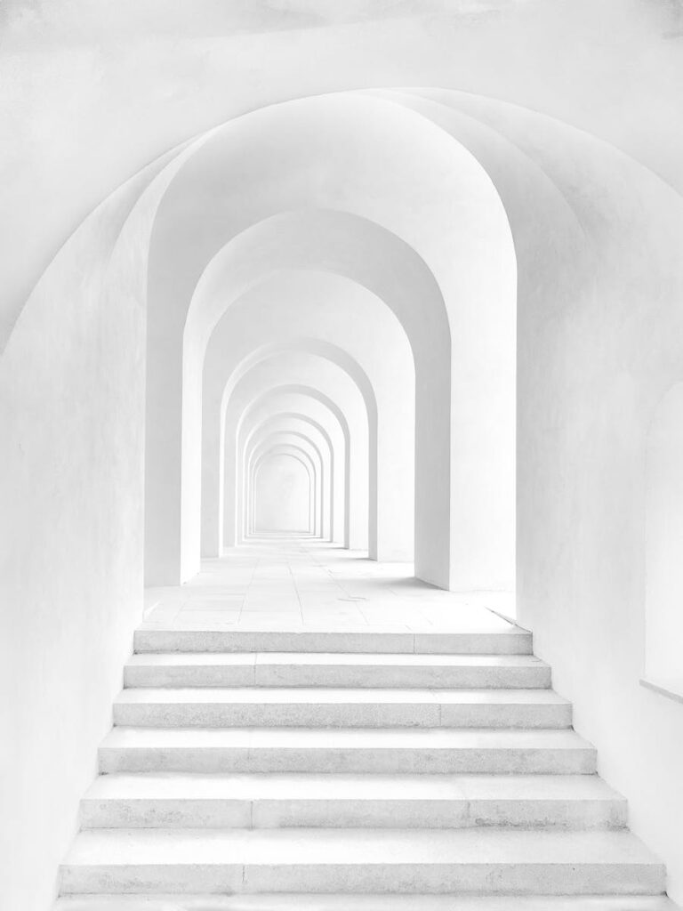 A minimalist white arched hallway in Prague with repetitive symmetry and soft lighting.