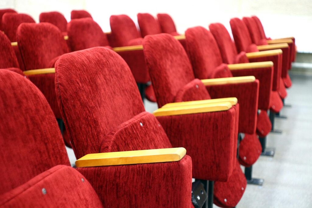 Empty auditorium rows of plush red velvet theater seats. Perfect for cinema and lecture hall themes.