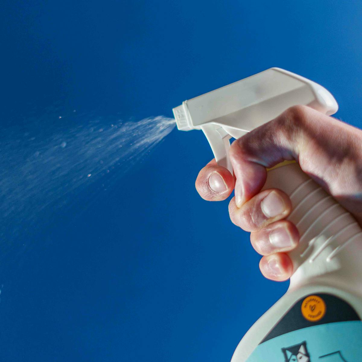 Close-up of a hand using pet-friendly cleaning spray, showcasing a high-quality product in action.