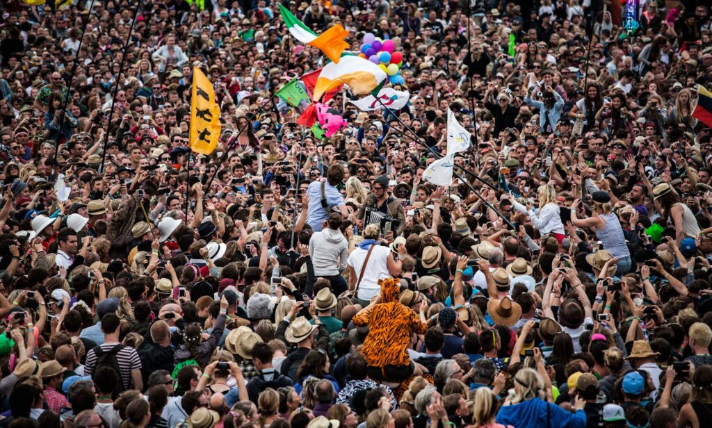 A lively festival scene with a large crowd, flags, and live music.