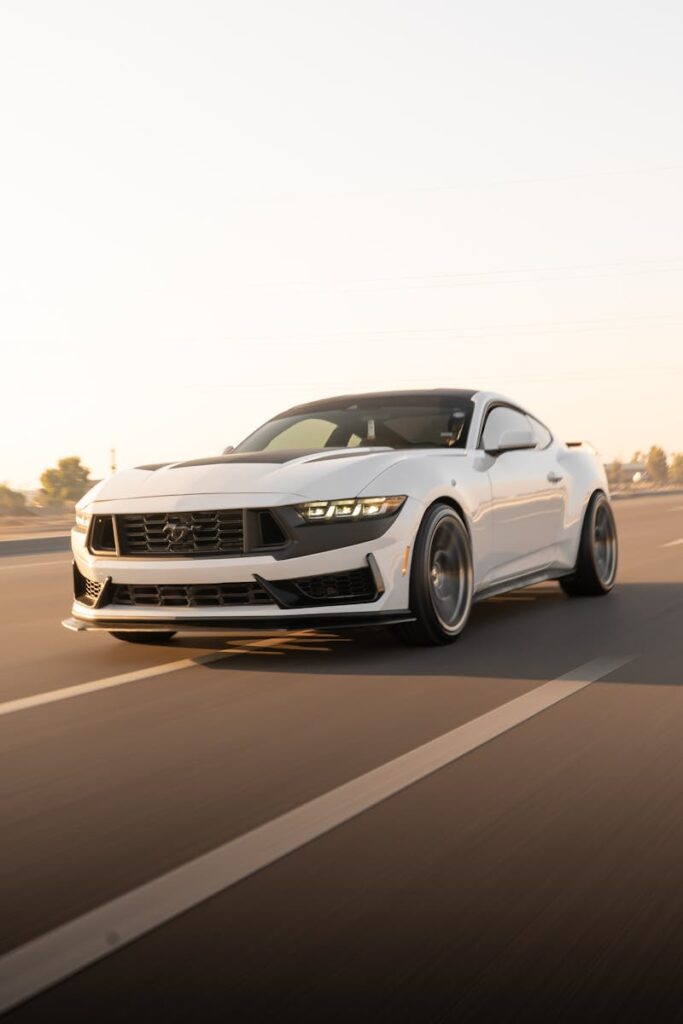 A high-performance white Mustang speeding down an empty highway at dusk, showcasing its sleek design.