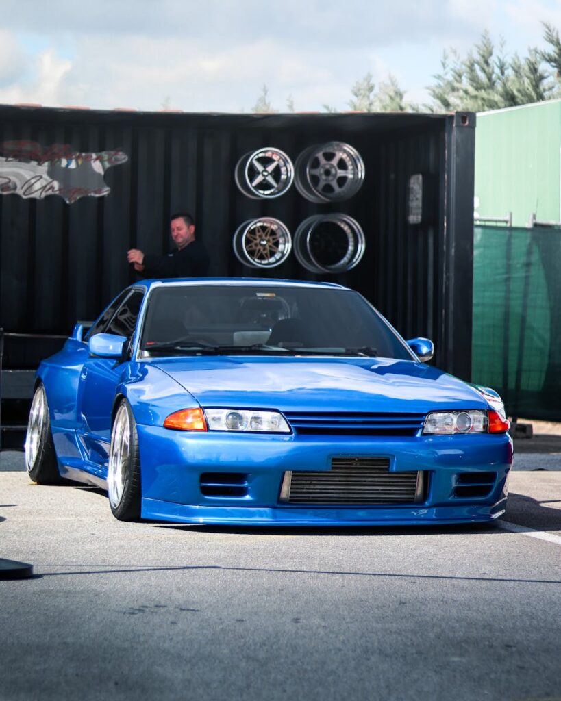 Blue Nissan GTR parked outdoors with car wheels and a person in the background.