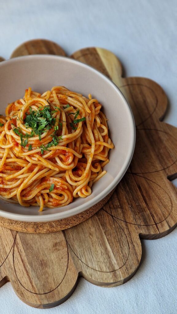 Bowl of spaghetti with tomato sauce and parsley on a wooden cutting board.