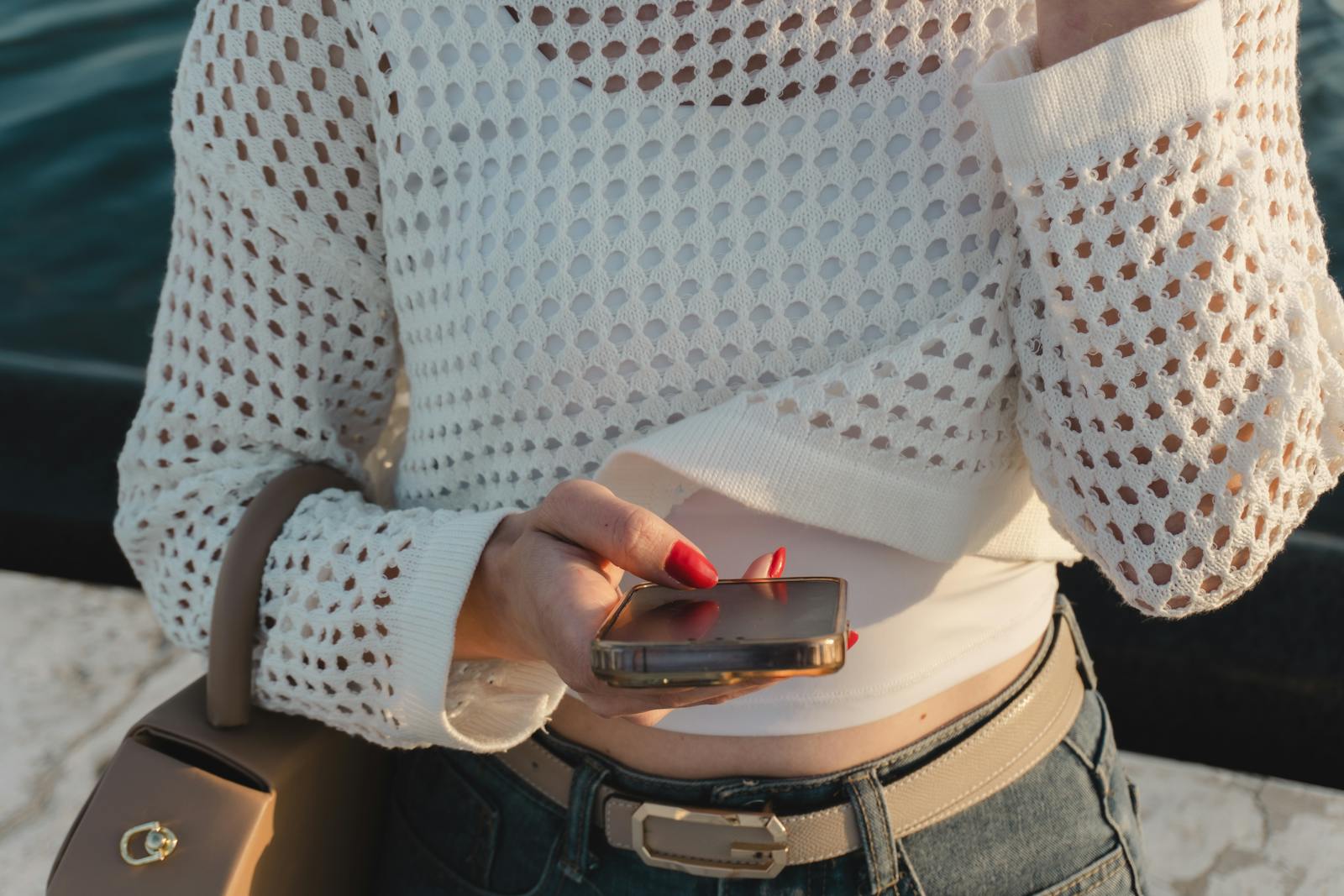 Woman in casual attire checks smartphone by river, stylish and modern.
