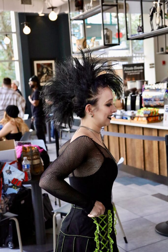 Gothic fashion enthusiast in a lively cafe setting with unique hairstyle and attire.
