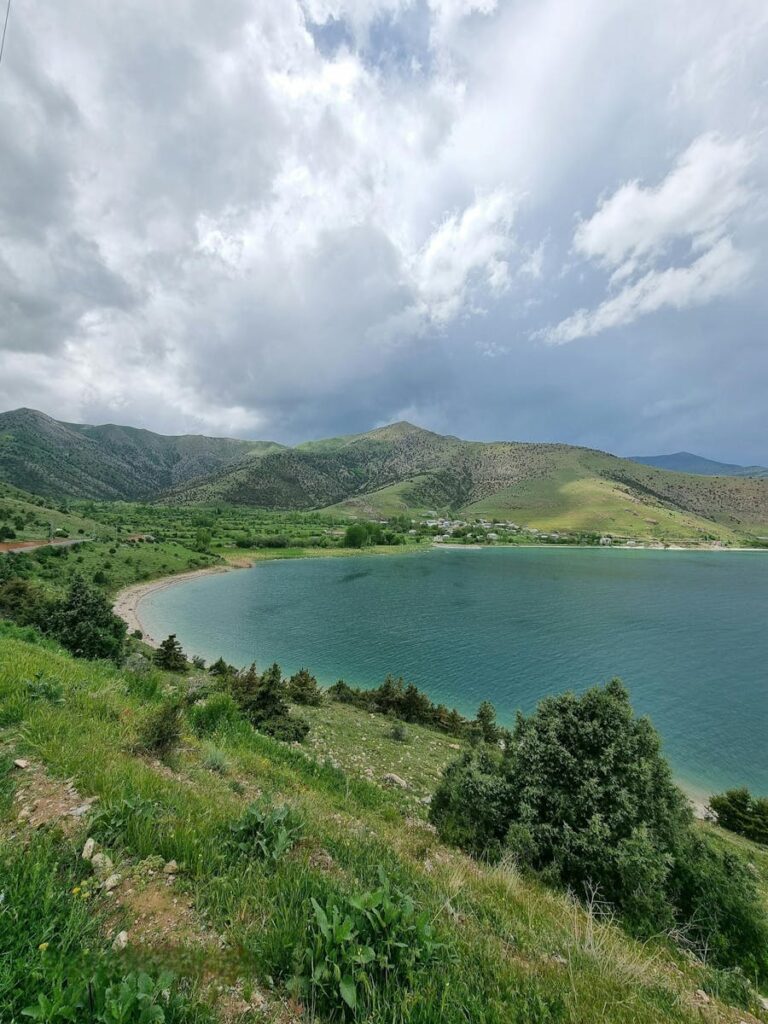 Peaceful mountain lake with lush greenery and dramatic clouds, perfect for nature lovers.