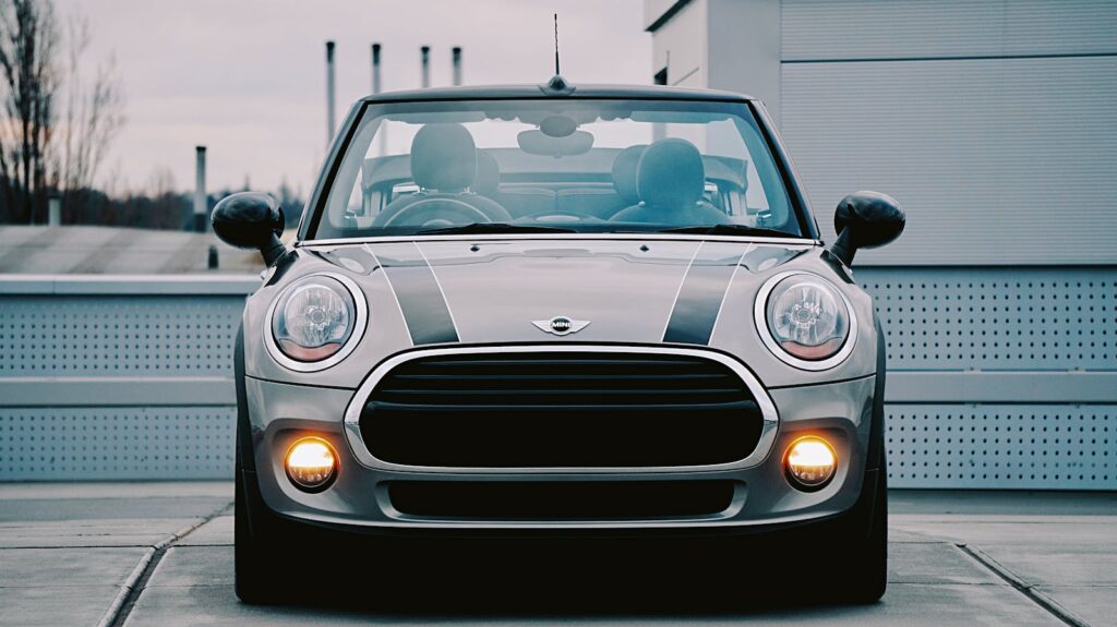 Sleek grey Mini Cooper convertible with headlights on, parked outdoors.