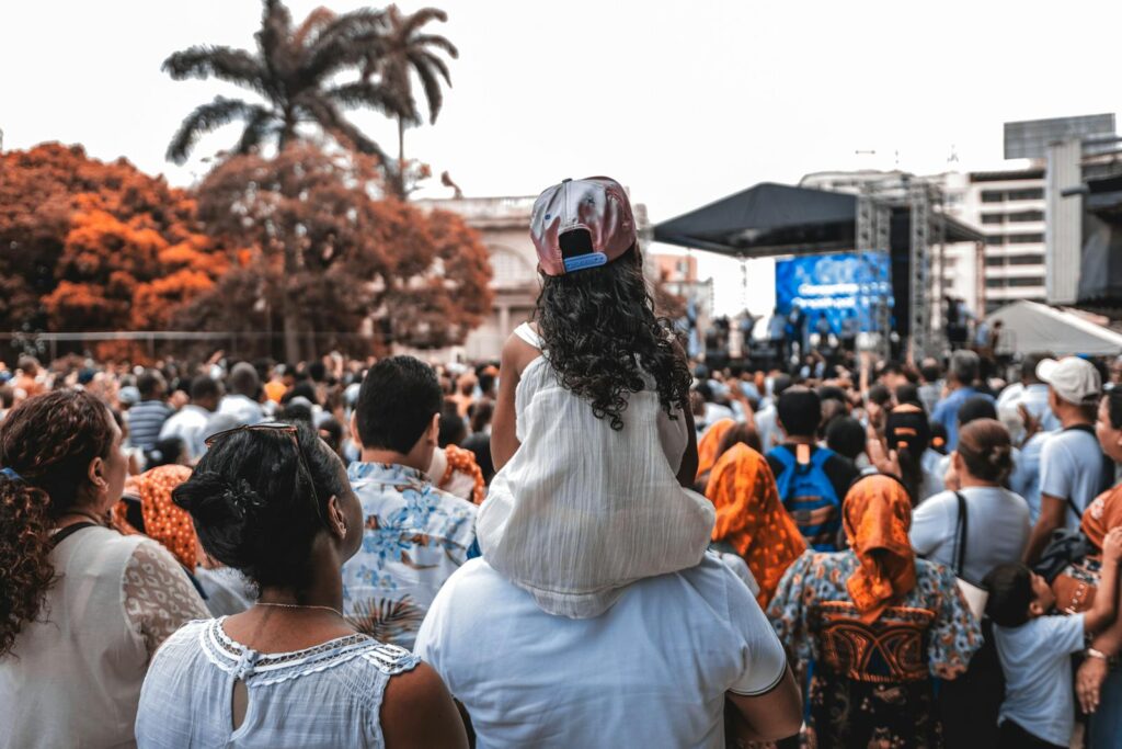 A diverse crowd gathered at an outdoor festival with families and music stage.