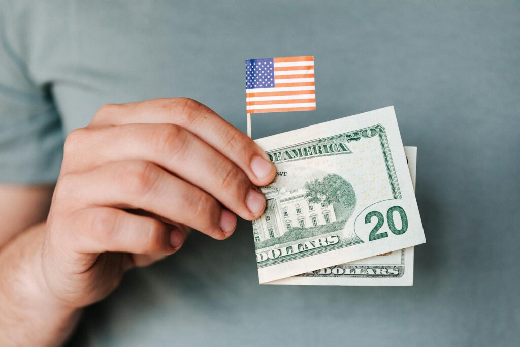 Close-up of a hand holding a US flag and twenty-dollar bill representing American finance.