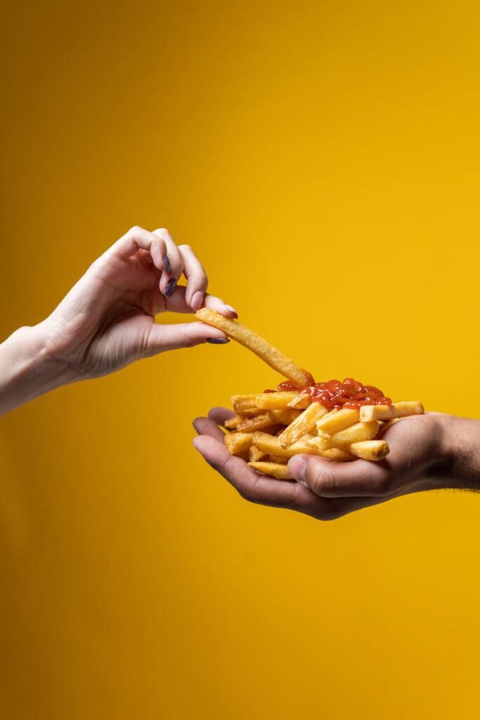 A close-up of hands sharing a delicious pile of french fries with ketchup against a yellow background.