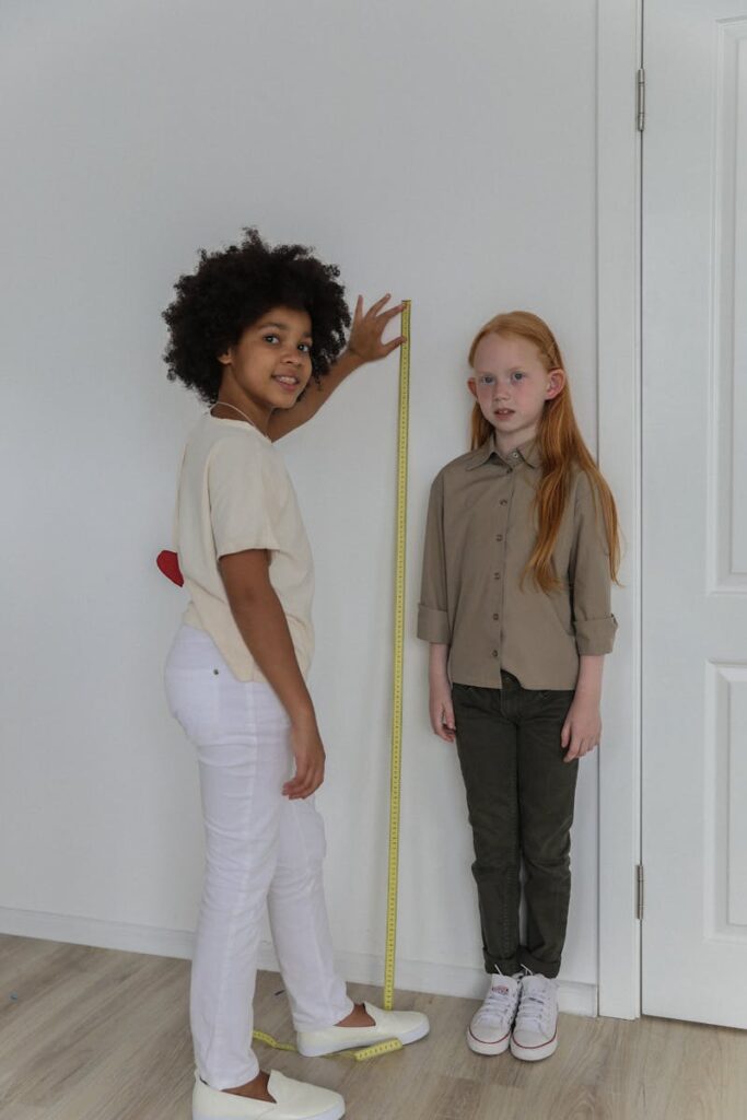 Two young girls measuring their heights with a tape indoors, smiling.