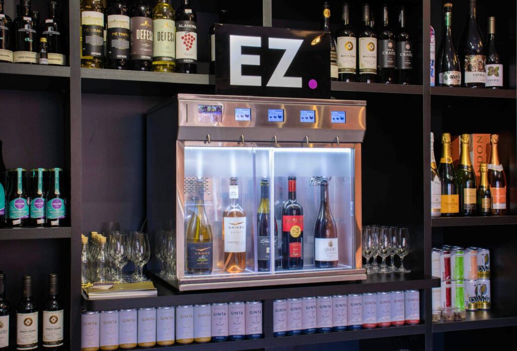 Elegant bar with wine dispenser and assorted drinks on shelves, showcasing modern liquor selection.