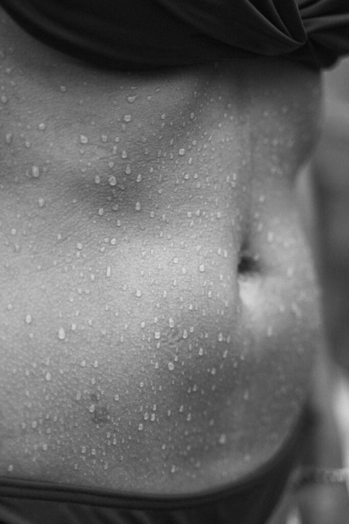 Black and white close-up of a torso with water droplets, highlighting skin texture.
