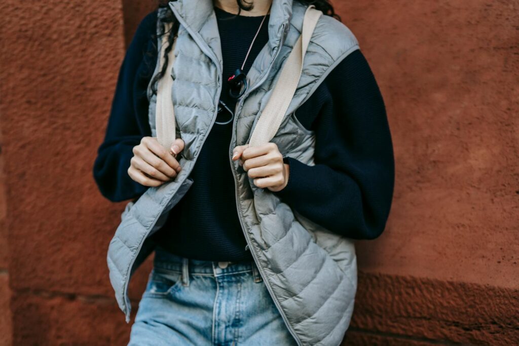 Crop unrecognizable female in trendy outfit and backpack leaning on stone wall while resting alone on street