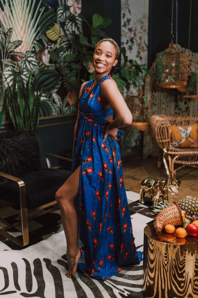 A woman in a vibrant dress poses in a stylish, African-themed interior setting.