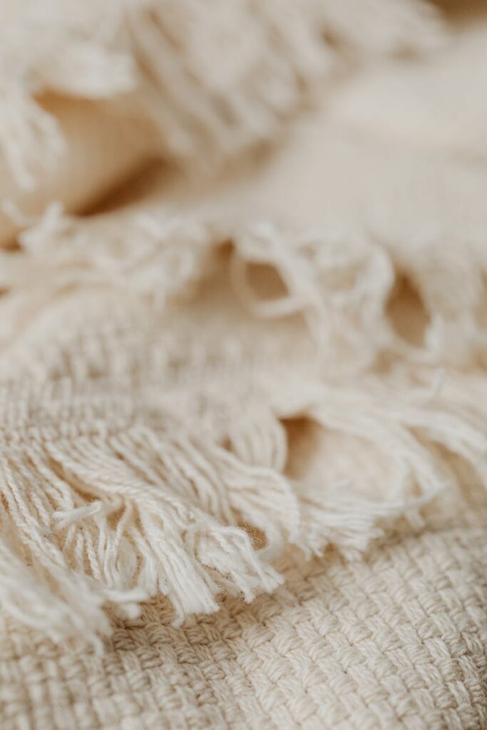 Detailed shot of cream woolen fabric with fringes, showcasing texture and softness.