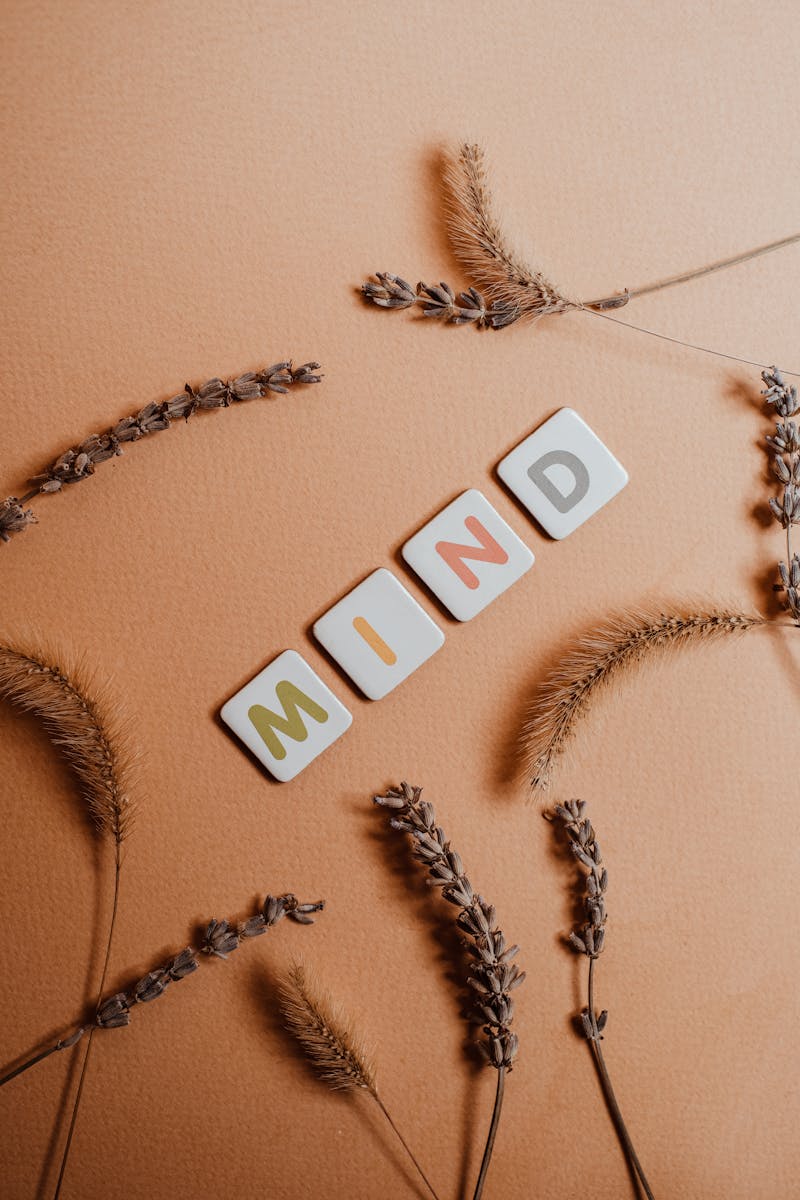 Tiles spelling 'MIND' among dry flowers on a warm backdrop, conveying mindfulness.