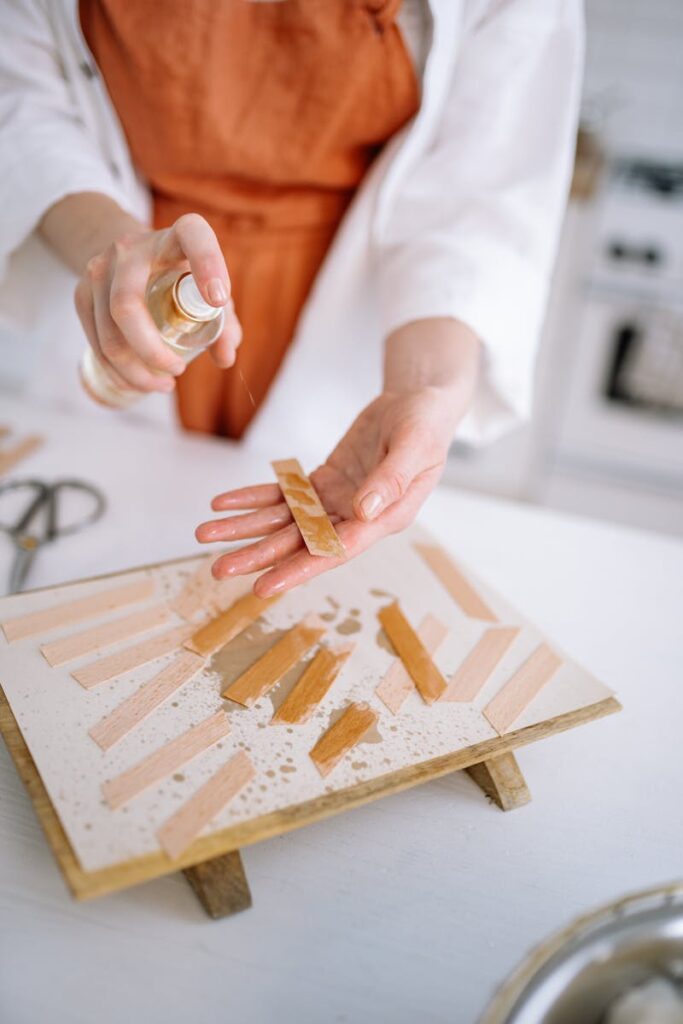 Person sprays fragrance on wooden strips with a bottle, creating a scented atmosphere.