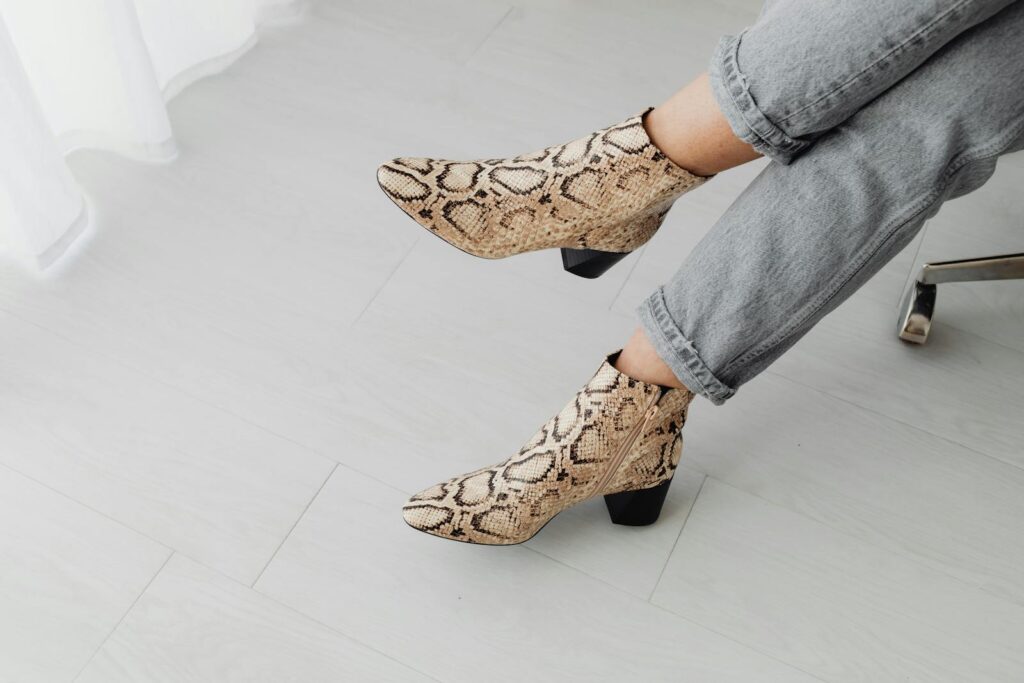 Stylish snake print boots paired with jeans on a light indoor floor.
