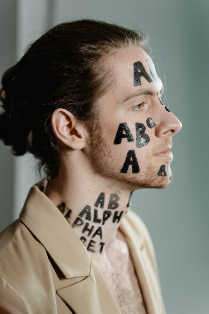 Close-up side view of a man with letters tattooed on his face, evoking a conceptual artistic theme.